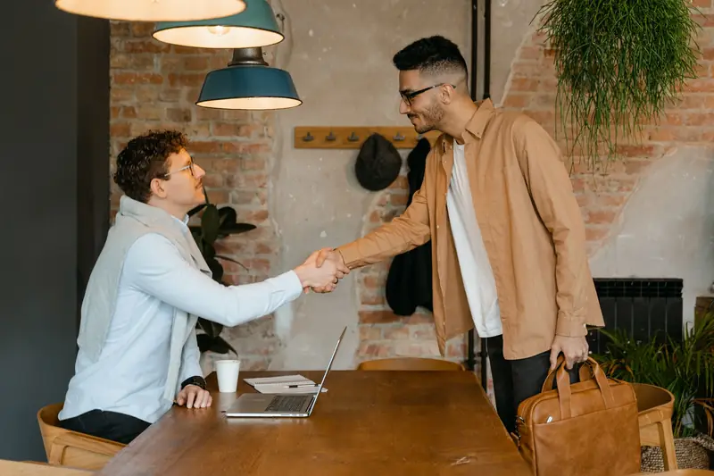 Twee mannen schudden elkaar de hand aan een tafel in een modern kantoor